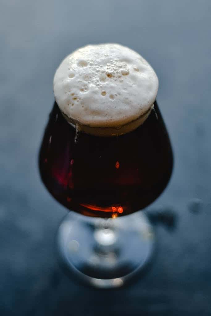 A close-up of a dark beer in a glass with a frothy head, showcasing the rich texture and color.